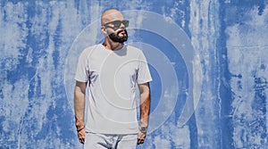 Male model with beard wearing white blank t-shirt on the background of an blue wall