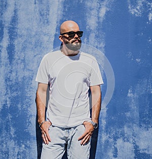 Male model with beard wearing white blank t-shirt on the background of an blue wall