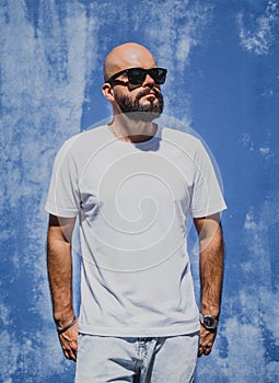 Male model with beard wearing white blank t-shirt on the background of an blue wall