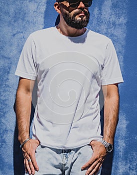 Male model with beard wearing white blank t-shirt on the background of an blue wall