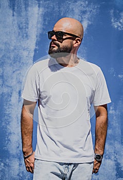 Male model with beard wearing white blank t-shirt on the background of an blue wall
