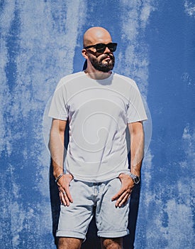 Male model with beard wearing white blank t-shirt on the background of an blue wall