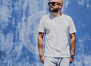 Male model with beard wearing white blank t-shirt on the background of an blue wall