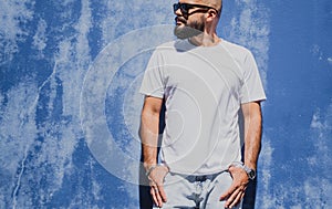 Male model with beard wearing white blank t-shirt on the background of an blue wall