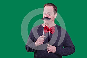 Male model holding fake mustache to face red bowtie photo booth prop captured a green screen background