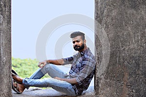 Male model sitting on a rock ledge looking at camera, Sion fort, Mumbai