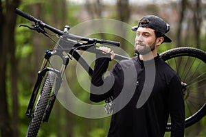 Male mountain biker carrying bicycle in the forest on a sunny day