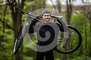 Male mountain biker carrying bicycle in the forest on a sunny day