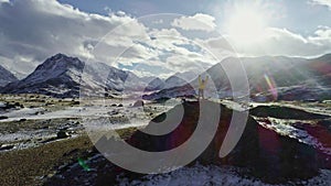 Male mountain climber raising hands with icepick on top of snowy peak