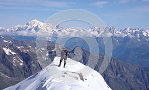 Male mountain climber on the summit of Gran Paradiso with a great view of Mont Blanc behind him