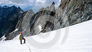 Male mountain climber takes a break on a high alpine glacier and looks at his way down and the descent route