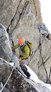 Male mountain climber traverses a tricky rock chimney on his way to a high alpine summit