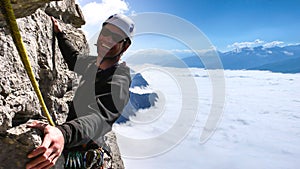 Male mountain guide smiling on a steep vertical rock climb in gorgeous surroundings high above a sea of clouds in the valley below
