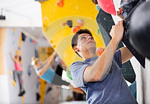 Male mountaineer climbing artificial rock wall without his belay indoors