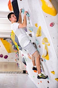 Male mountaineer climbing artificial rock wall without his belay indoors