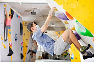 Male mountaineer in protective mask climbing artificial rock wall without his belay