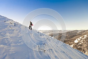 A male mountaineer walking uphill on a glacier. Mountaineer reaches the top of a snowy mountain in a sunny winter day.