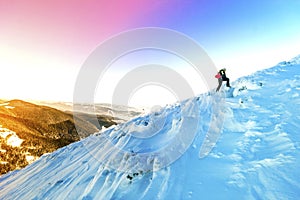 A male mountaineer walking uphill on a glacier. Mountaineer reaches the top of a snowy mountain in a sunny winter day.