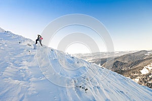 A male mountaineer walking uphill on a glacier. Mountaineer reaches the top of a snowy mountain in a sunny winter day.