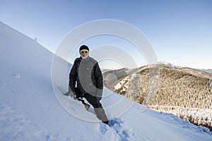 A male mountaineer walking uphill on a glacier. Mountaineer reaches the top of a snowy mountain in a sunny winter day.