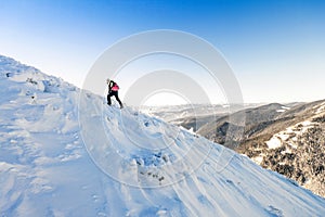 A male mountaineer walking uphill on a glacier. Mountaineer reaches the top of a snowy mountain in a sunny winter day.