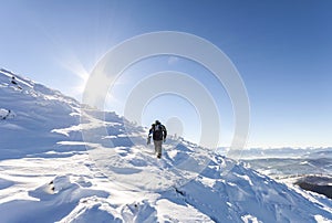 A male mountaineer walking uphill on a glacier. Mountaineer reaches the top of a snowy mountain in a sunny winter day.