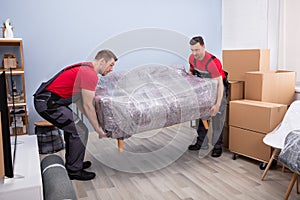 Male Movers Carrying Wrapped Sofa In New House