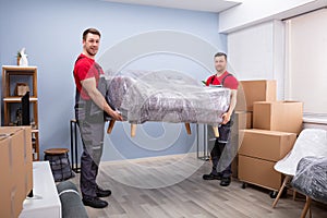 Male Movers Carrying Wrapped Sofa In New House