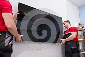 Male Movers Fixing The Large LCD Television On Wall