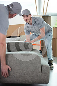 male movers placing sofa on hardwood floor at home