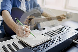 Male music arranger composing song on midi piano and audio equipment in digital recording studio. Man plays guitar and