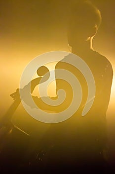 Male musician with a cello on the stage lit by a yellow honey light from behind. reportage