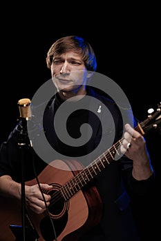 Male musician with guitar in hands playing and posing on black background