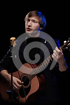 Male musician with guitar in hands playing and posing on black background