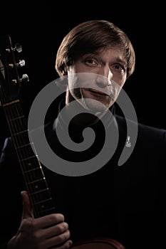 Male musician with guitar in hands playing and posing on black background