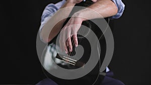 male musician with a guitar in hands rotates in a circle on a dark background, medium plan