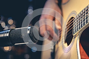 Male musician playing acoustic guitar behind microphone in recording studio.