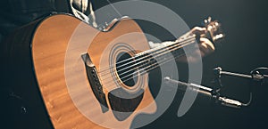 Male musician playing acoustic guitar behind microphone in recording studio.