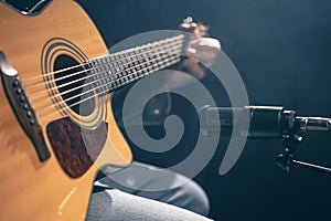 Male musician playing acoustic guitar behind microphone in recording studio.