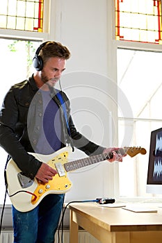 Male musician playing electric guitar in home studio