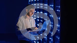 Male network engineer doing a system check standing in the server room with his laptop. At data center men server