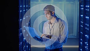 Male network engineer doing a system check standing in the server room with his laptop. At data center men server