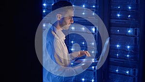 Male network engineer doing a system check standing in the server room with his laptop. At data center men server