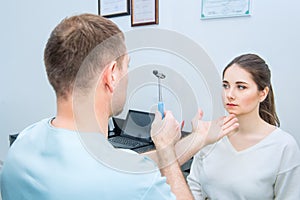 Male neurologist doctor inspecting young female patient`s nervous system using a hammer. Neurological physical examination. Helth