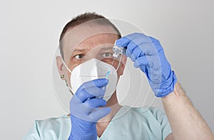 Male nurse with face mask and blue gloves, holding syringe with needle and covid-19 vaccine vial. Medical concept