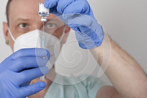 Male nurse with face mask and blue gloves, holding syringe with needle and covid-19 vaccine vial. Medical concept