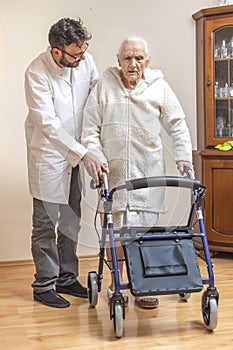 Male nurse helps the old lady to walk with the help of a walker, a balcony.
