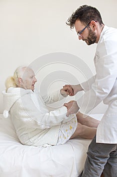 Male nurse helps to get up from the bed of an old woman.