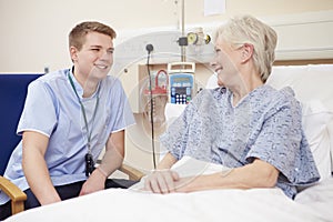 Male Nurse Sitting By Female Patient's Bed In Hospital