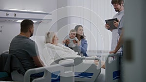 Male nurse with tablet computer talks to female senior patient resting in bed